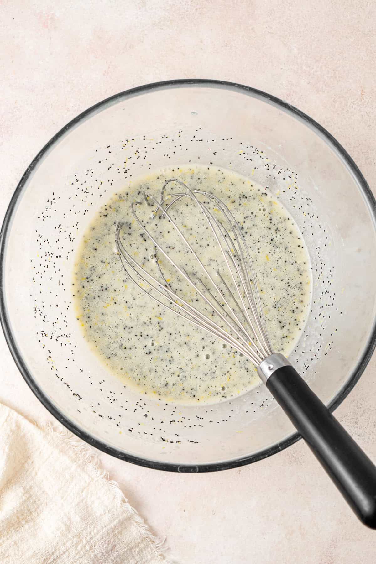 Adding the lemon and poppy seeds to the bowl with the whisk.