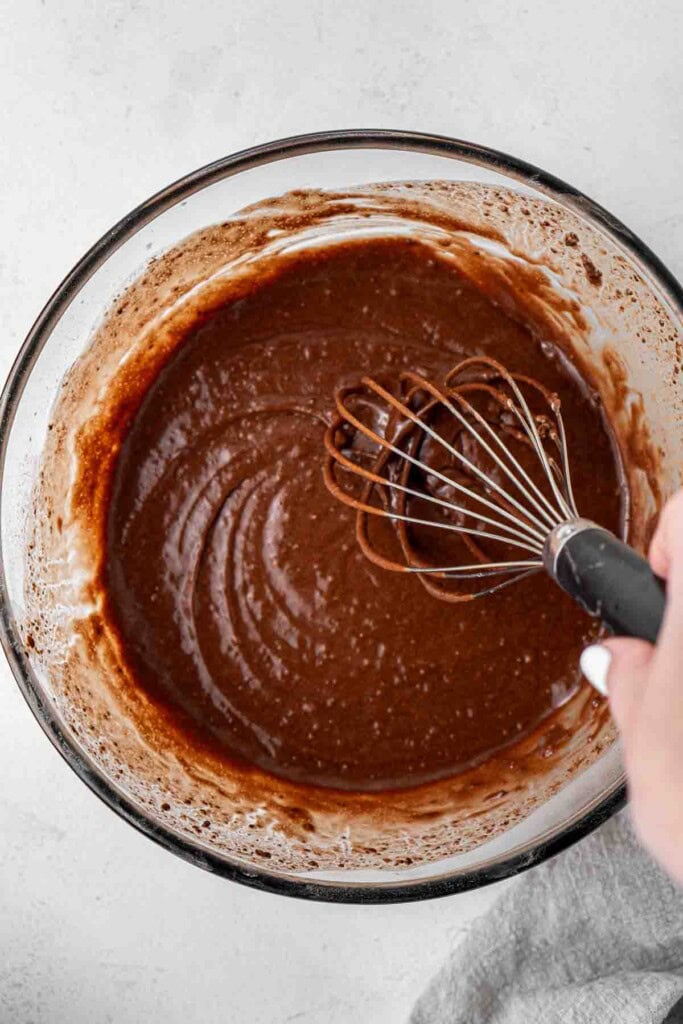 Whisking together the vegan chocolate cupcake batter in a glass bowl.