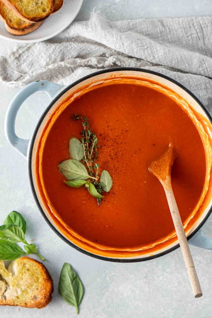 Blended tomato soup in the pot with herbs and a wooden spoon.
