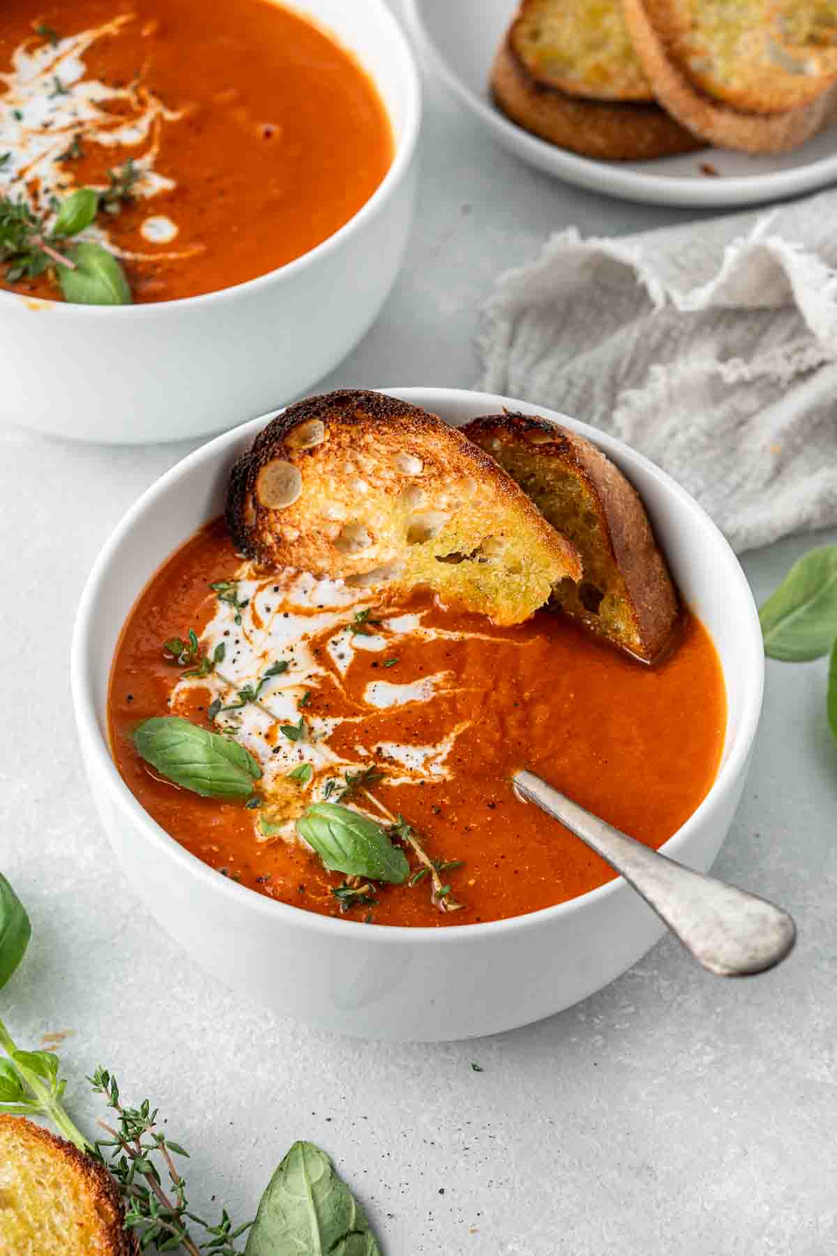 Close up of a bowl of tomato soup with toasted bread and a spoon.