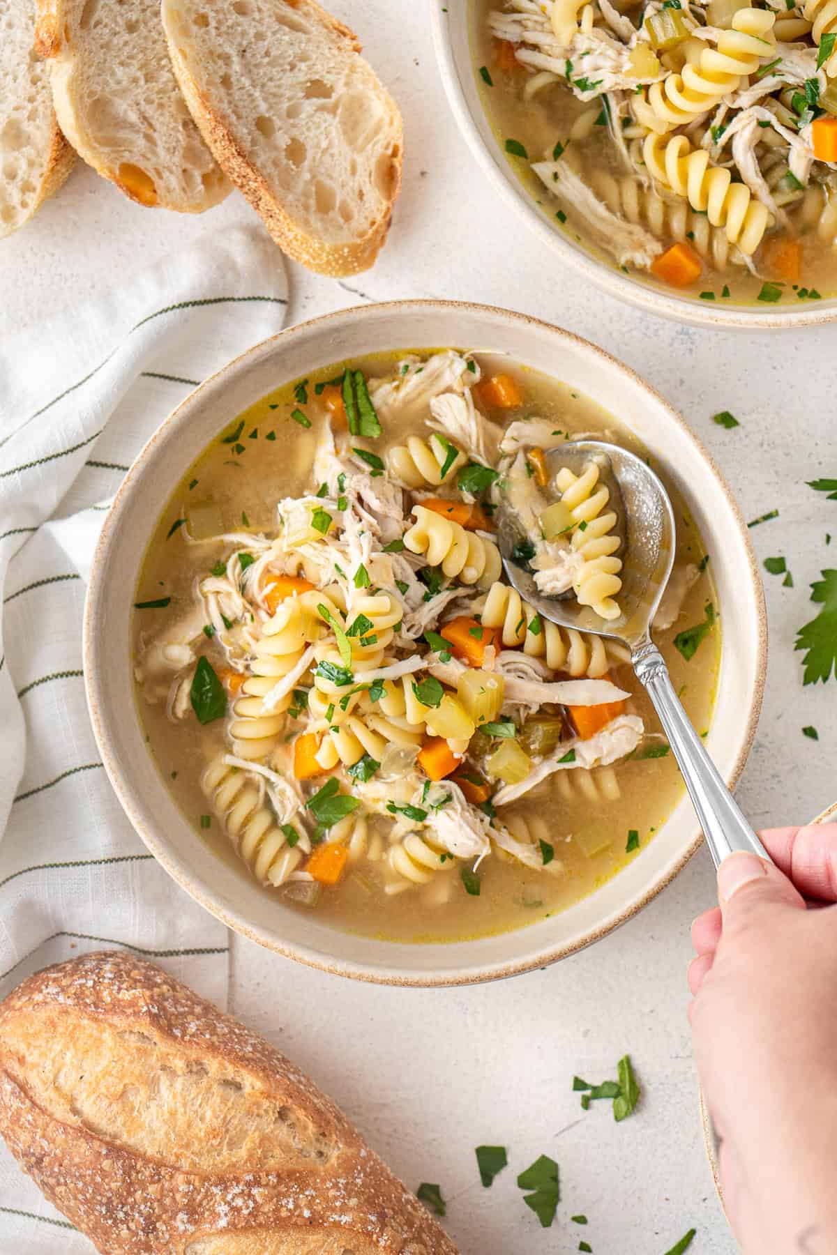 A hand taking a spoonful of chicken noodle soup.