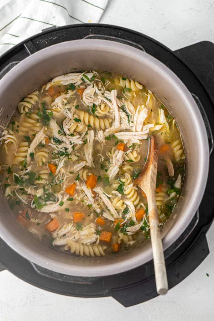 A wooden spoon in the pressure cooker with the finished chicken noodle soup.