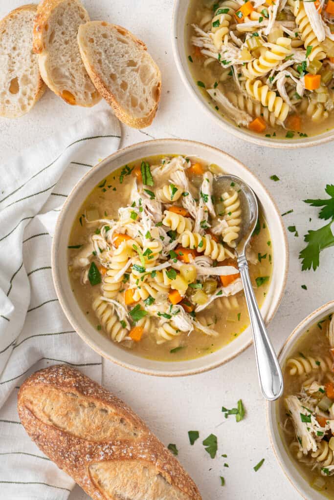 Chicken noodle soup served into bowls with fresh bread and a spoon.
