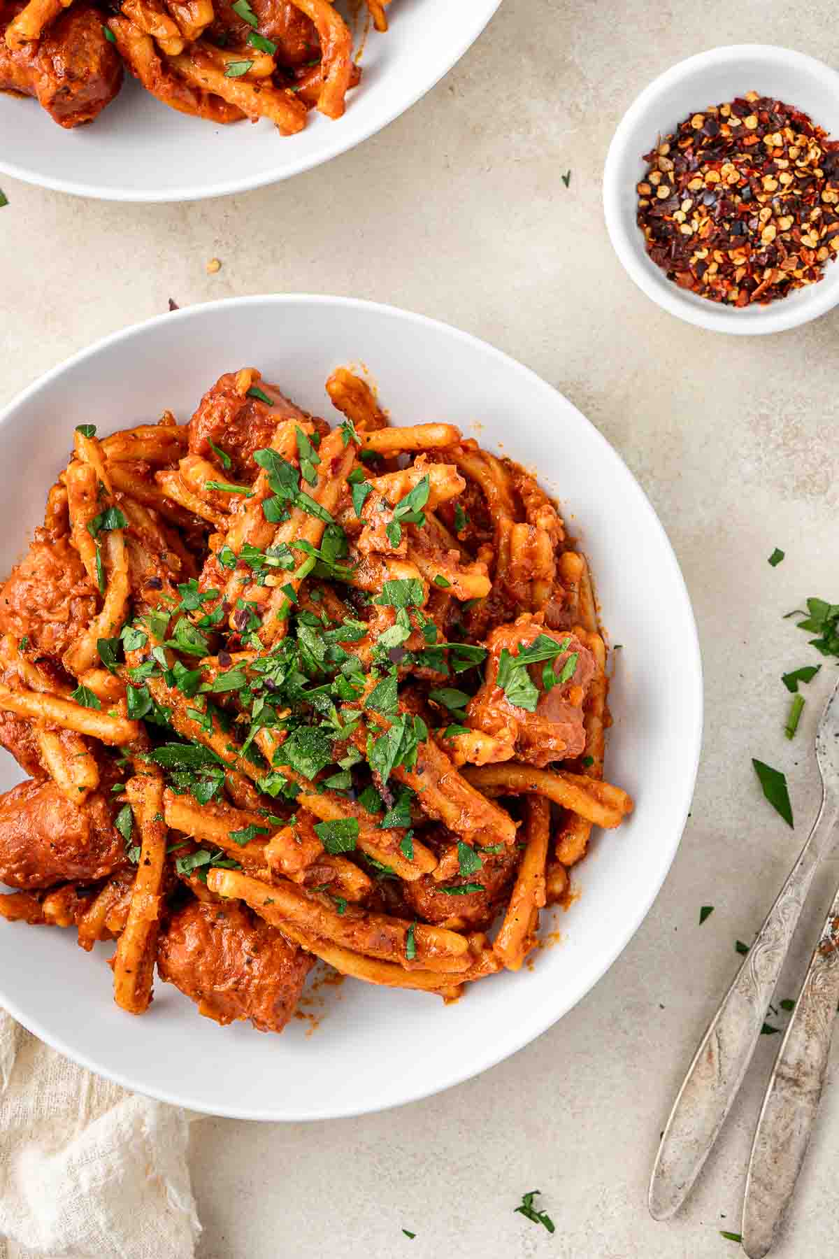 A bowl of spicy sausage pasta with fresh parsley.