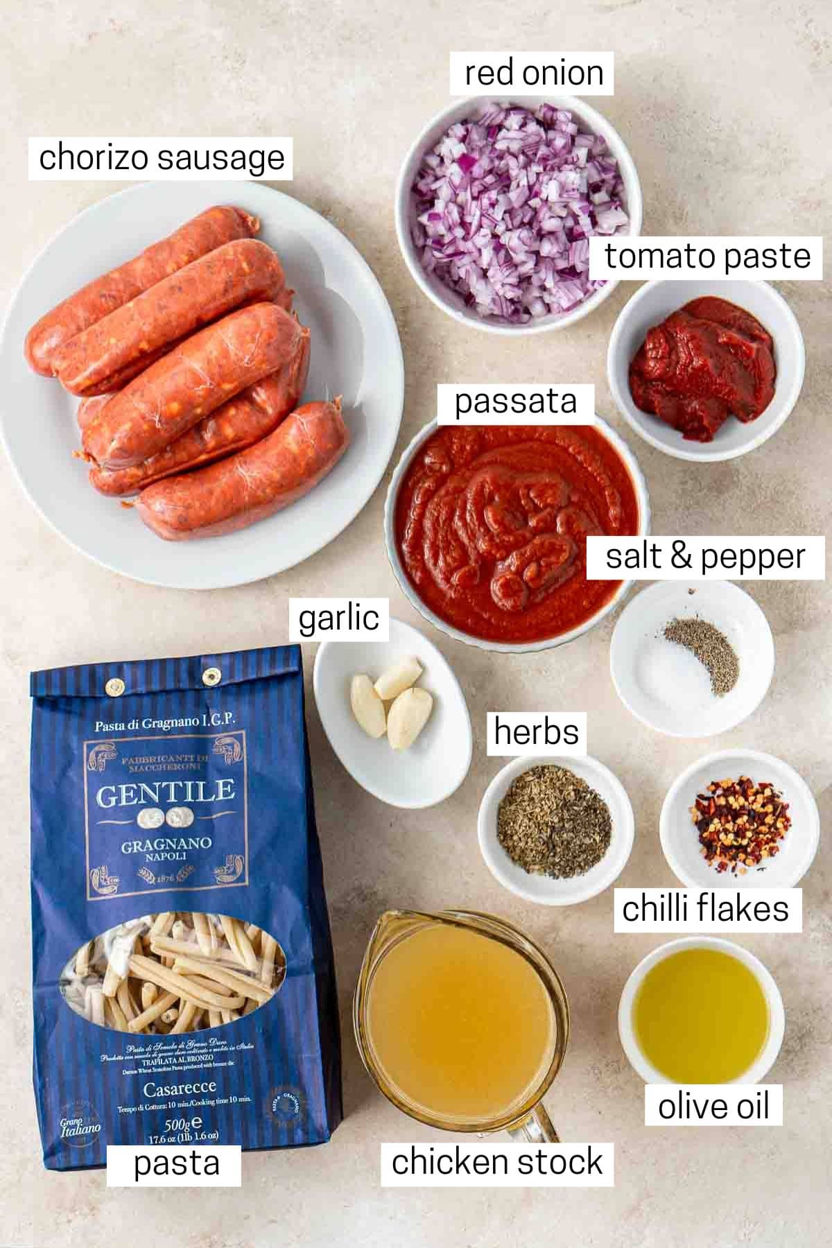 All ingredients needed to make spicy sausage pasta laid out in small bowls.