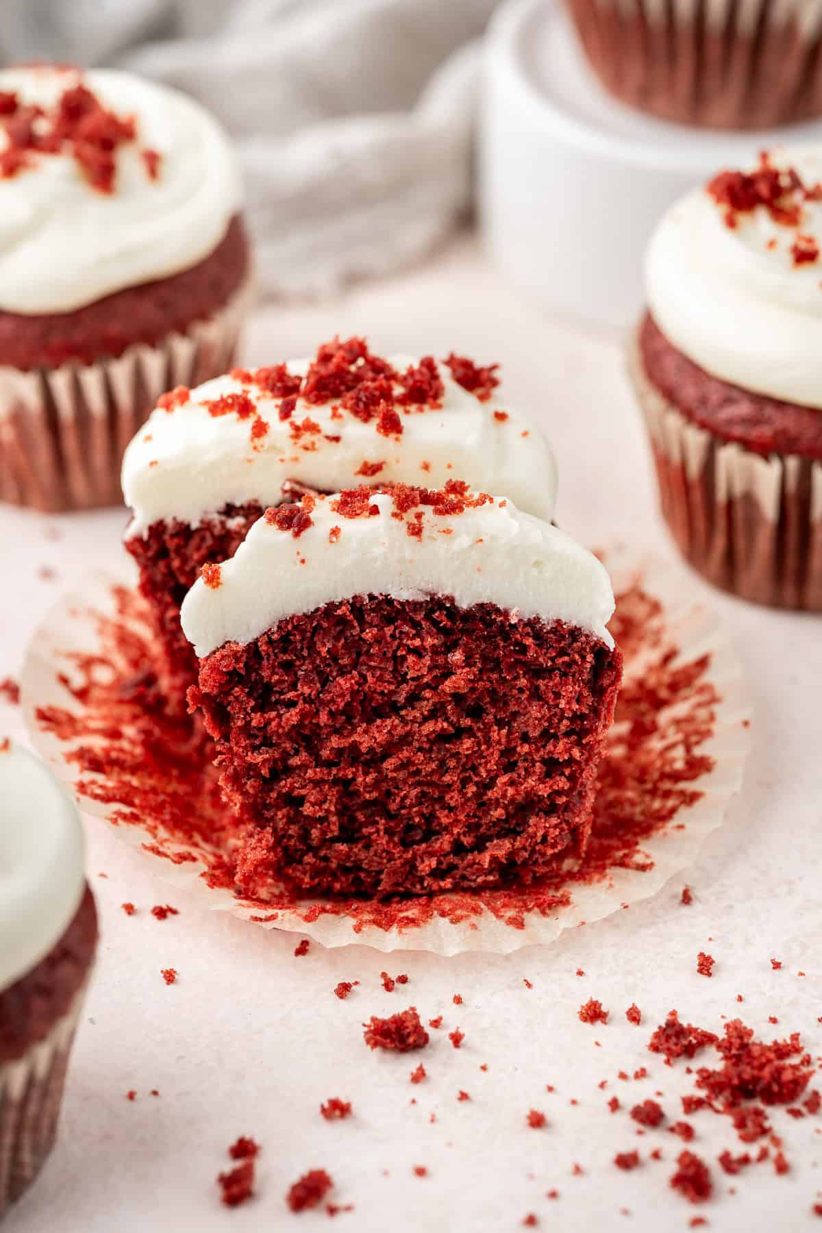 Vegan red velvet cupcakes with cream cheese frosting cut in half to show the vibrant cake colour.