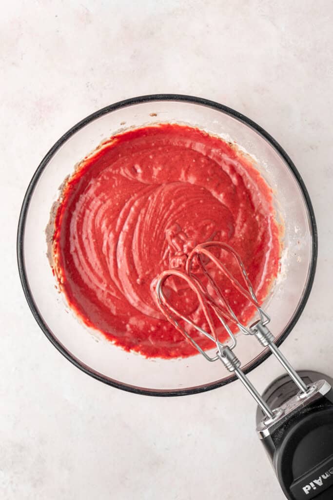 Mixing in the red colouring to the batter in a glass bowl.