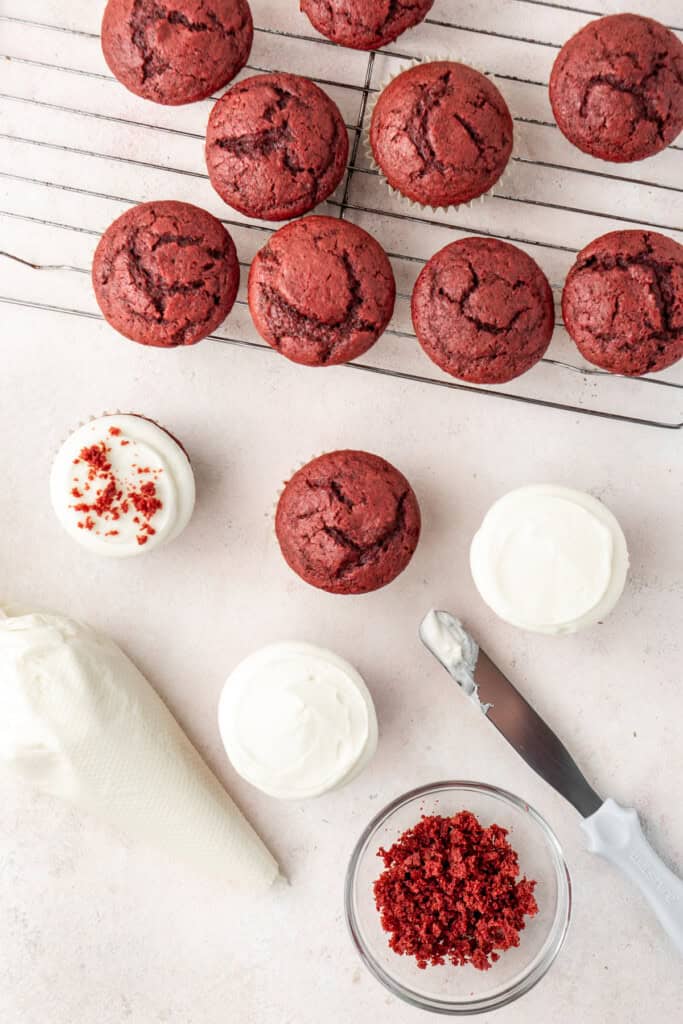 Frosting the red velvet cupcakes with cream cheese frosting.