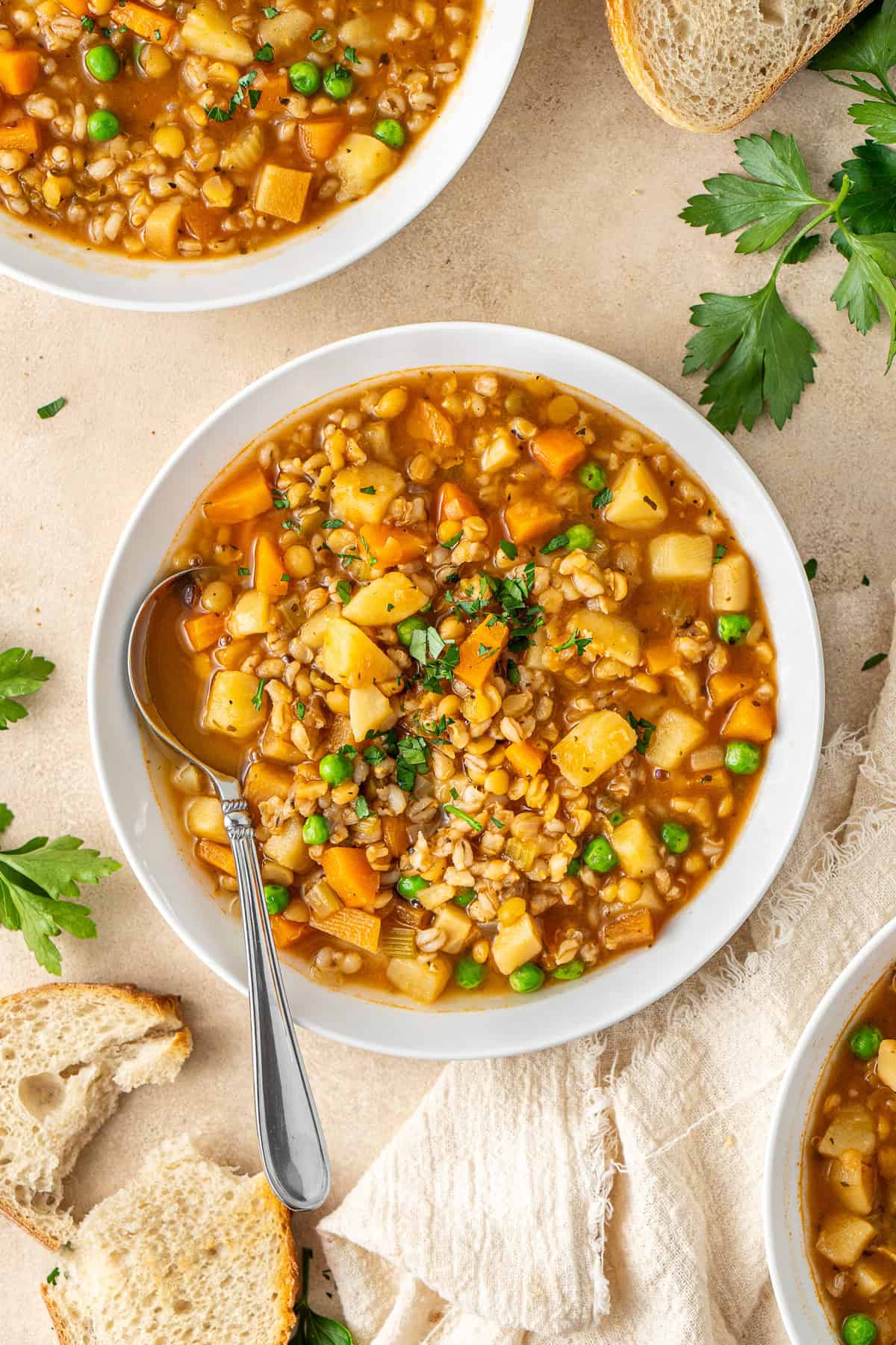 Vegetable soup with barley and lentils served into bowls with a spoon.