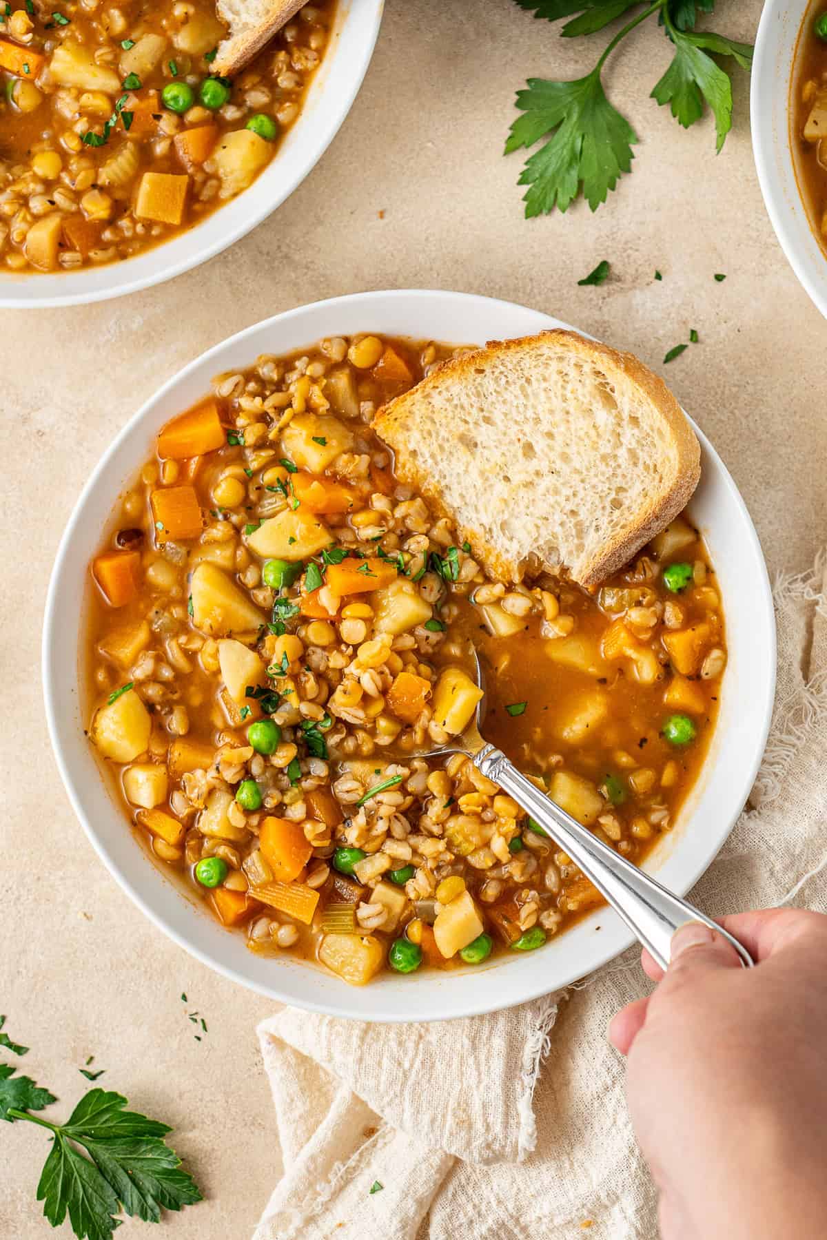 A hand taking a spoon of soup with a slice of crusty bread.