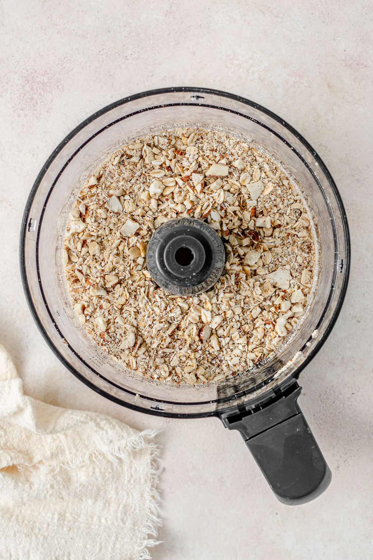 The oats and nuts in the bowl of the food processor.