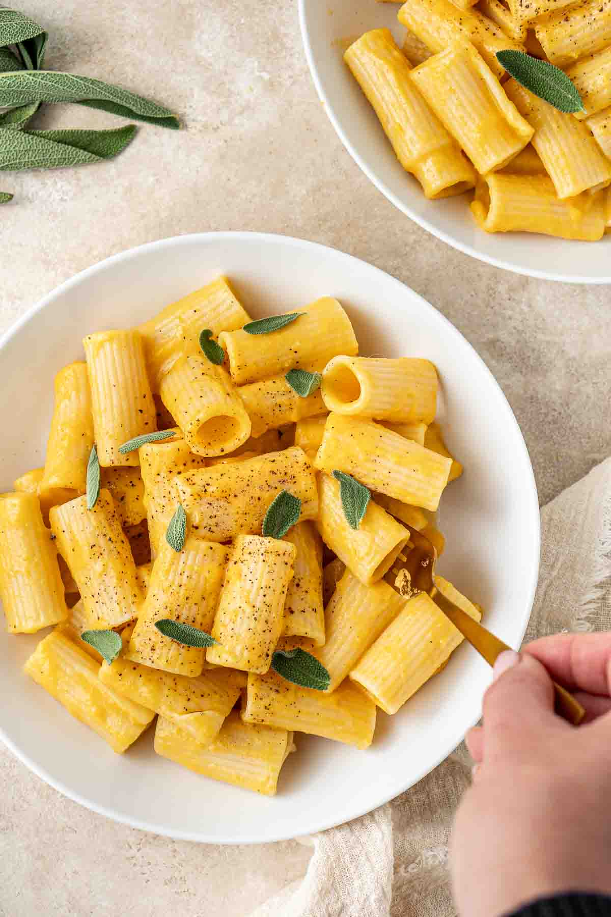Bowl of creamy vegan pumpkin pasta with sage and pepper.