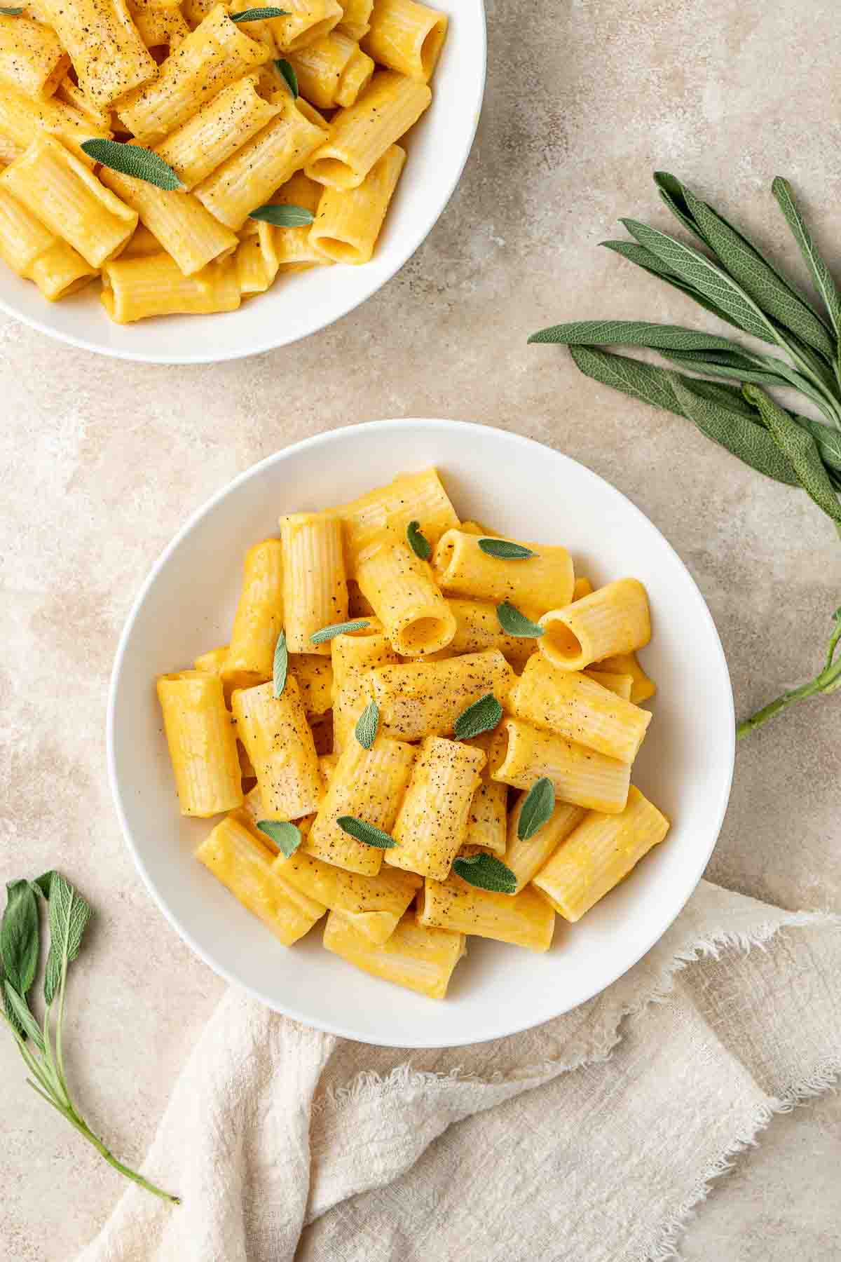 Vegan pumpkin pasta in white bowls topped with sage and pepper.