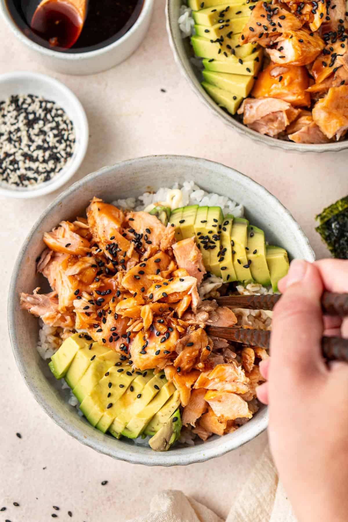 A hand using chopsticks to get a bite of teriyaki salmon and avocado.