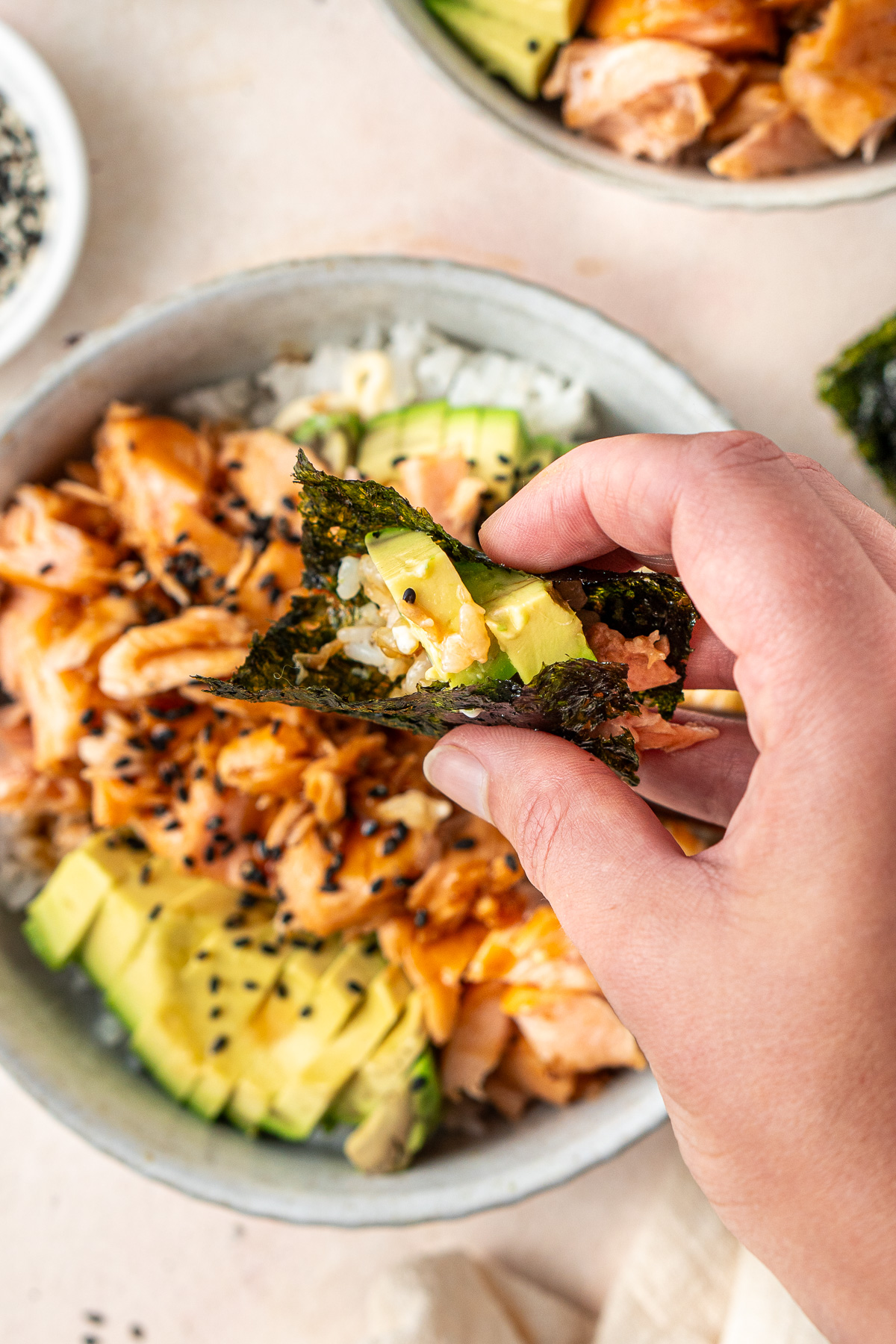 A hand taking a bite of the sushi bowl using a piece of seaweed. 