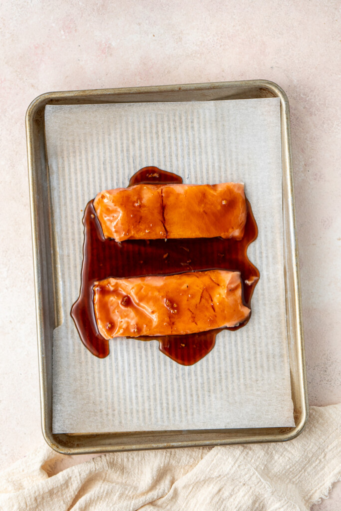 The salmon coated in the teriyaki sauce on a baking tray ready for the oven.