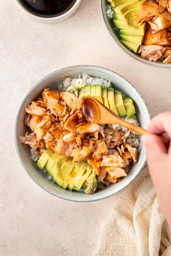 Spooning more teriyaki sauce over the salmon and avocado bowl.