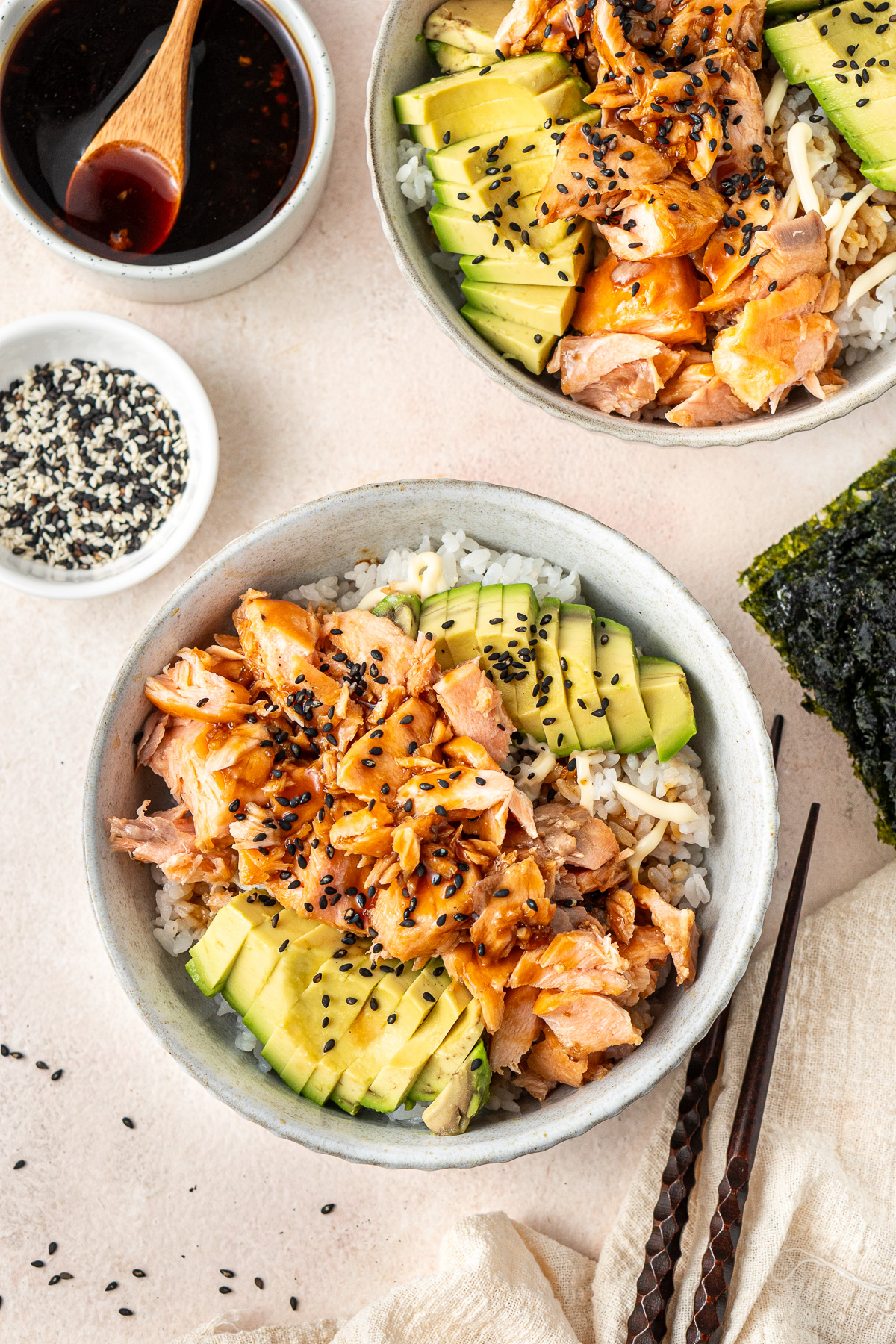 Two salmon and avocado rice bowls served up and garnished with black sesame seeds. 