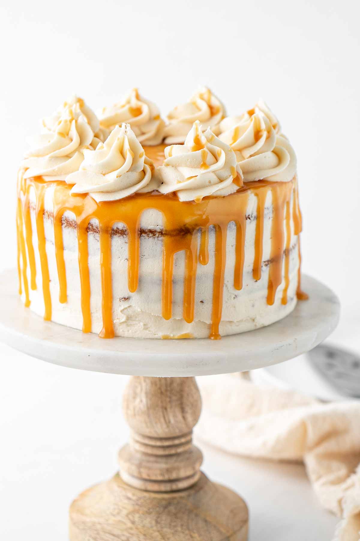 A vegan caramel cake with a caramel drip and swirls of buttercream frosting on top on a cake stand.