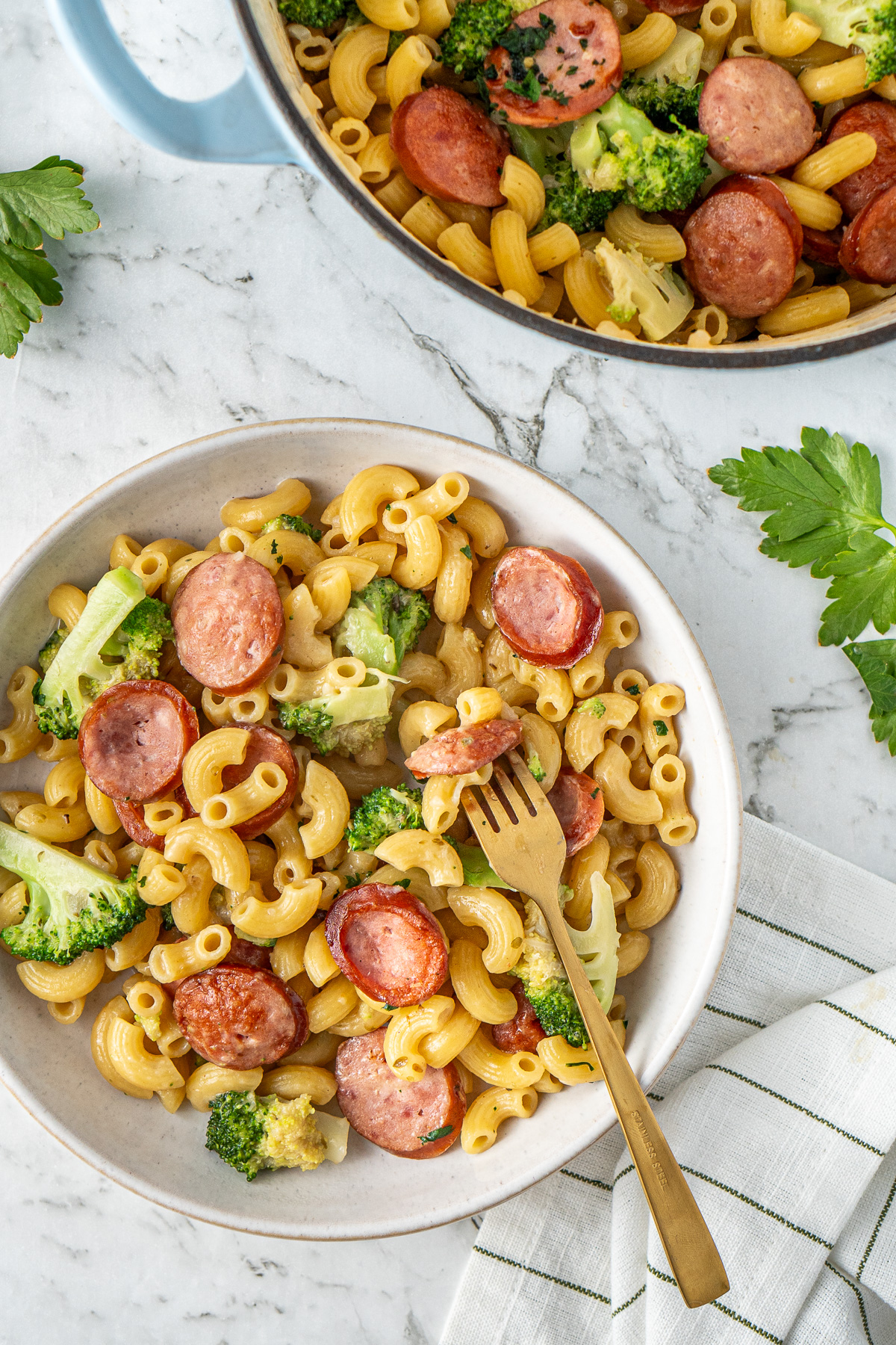 A fork taking a bite of sausage and broccoli pasta in a bowl.