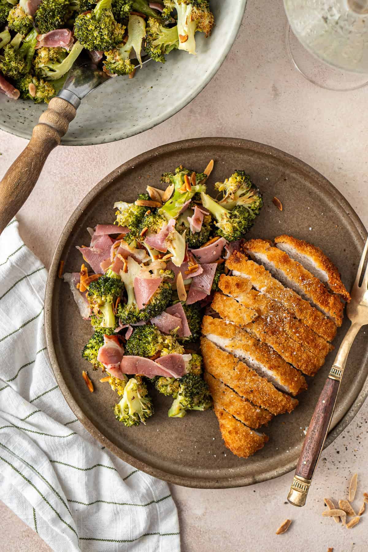 Roasted broccoli salad served up on a plate with a chicken schnitzel.