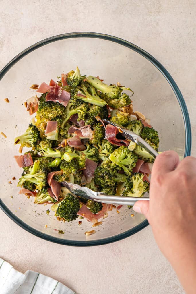Tossing the salad with tongs in a glass bowl.