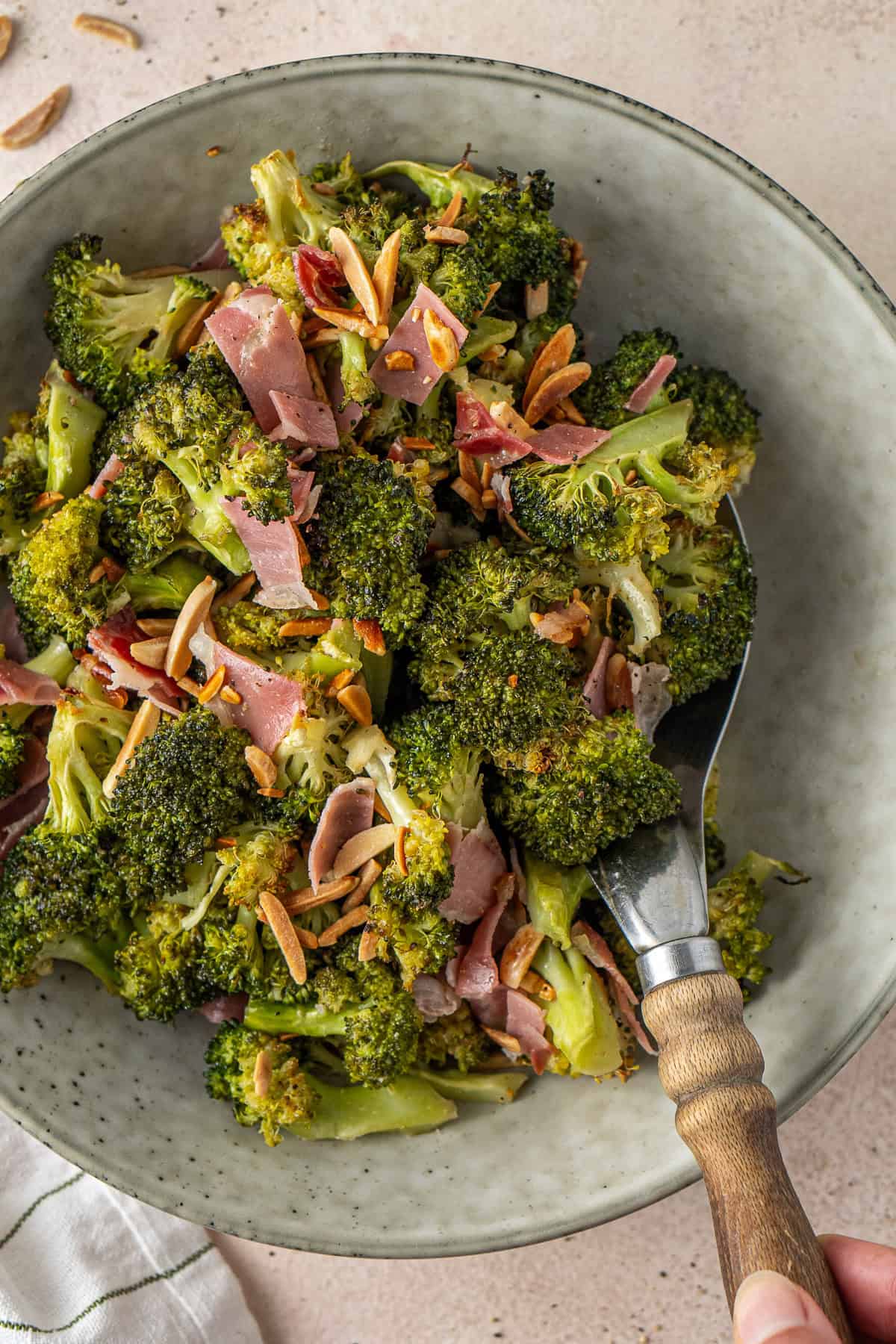 Close up of a spoon scooping up some roasted broccoli salad from a bowl.