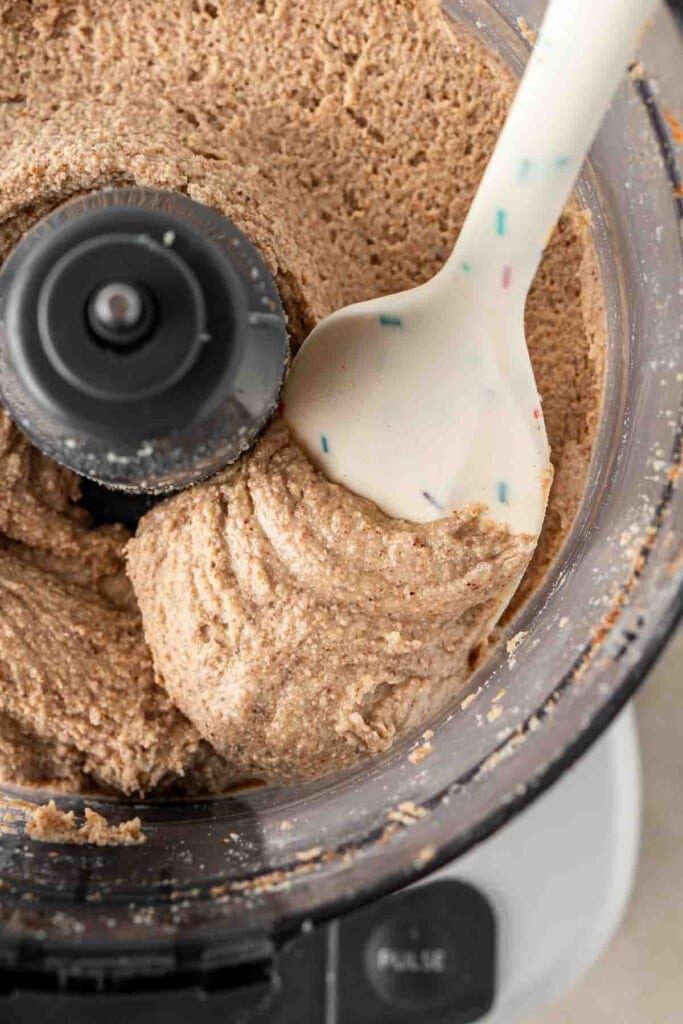 A spatula scooping almond butter from the food processor. 