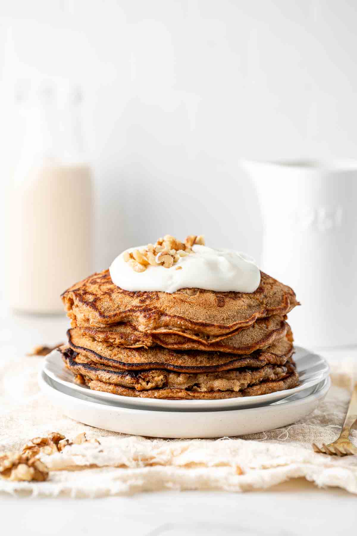 A stack of carrot cake pancakes on a white plate topped with yoghurt.