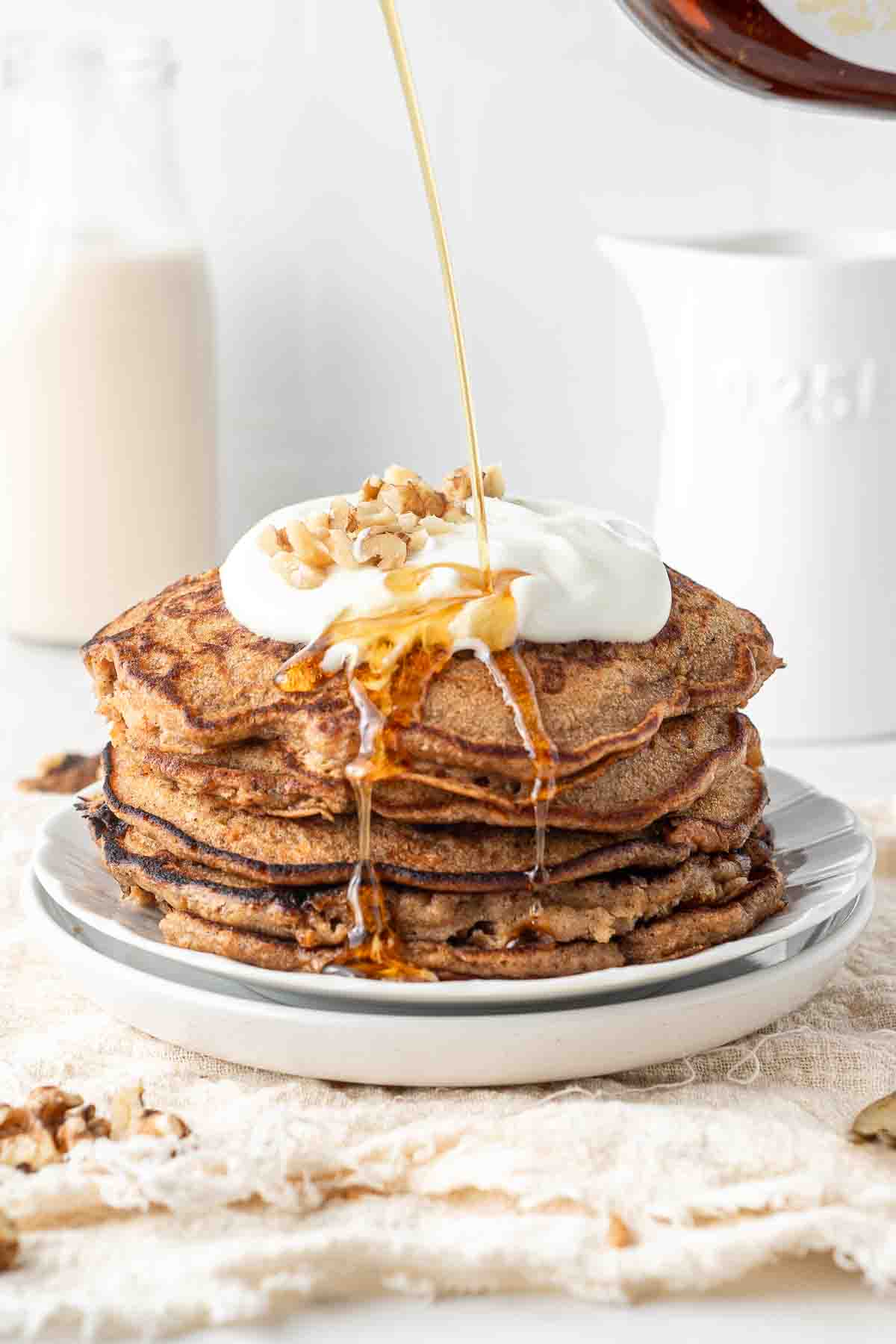 A stack of carrot cake pancakes with maple syrup being drizzled.