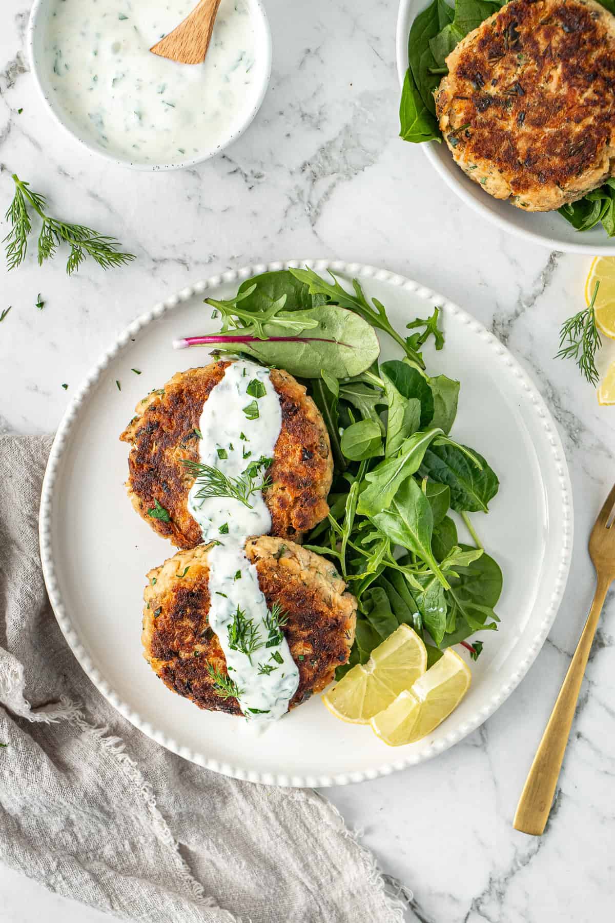 Salmon patties served on a plate with yoghurt sauce, salad and fresh lemon.