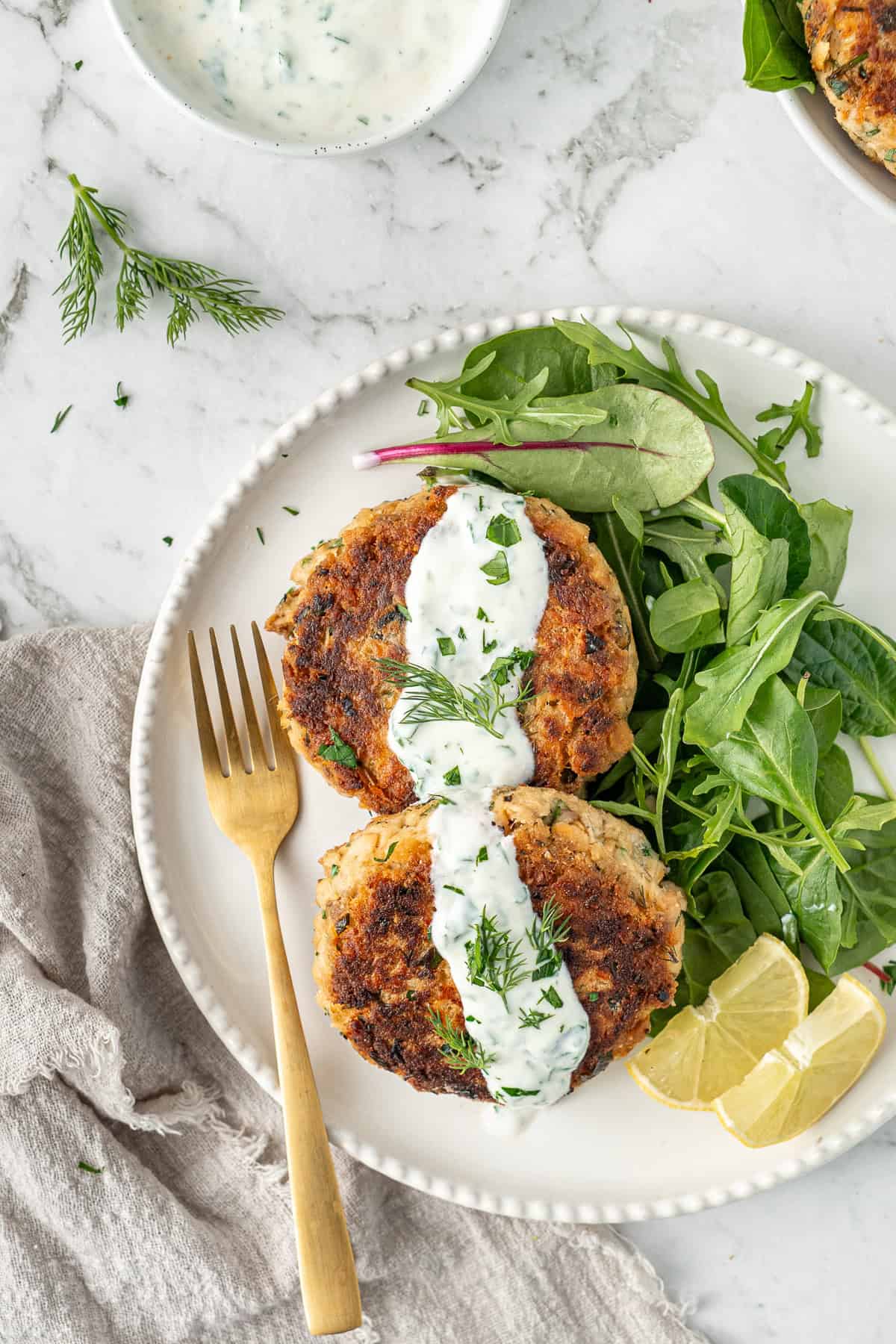 Healthy salmon patties with a yoghurt sauce on a plate with salad and a fork.