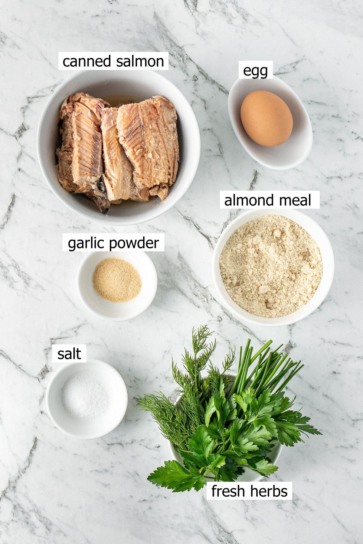 All ingredients needed to make salmon patties with canned salmon laid out in bowls.