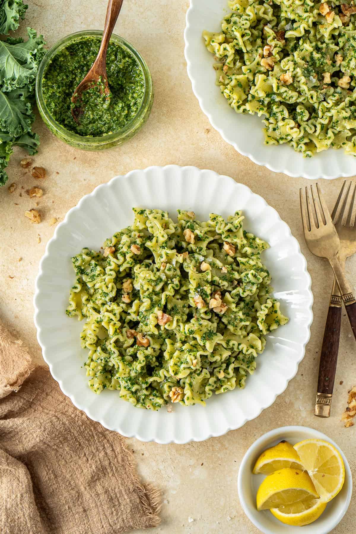 The kale walnut pesto pasta served in white plates on a brown background with lemon wedges.
