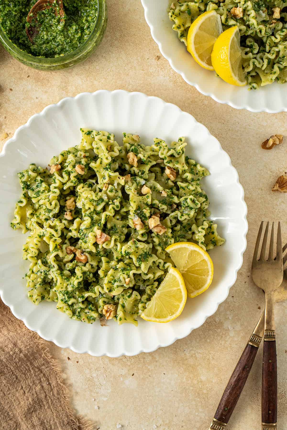 Kale pesto pasta served in a white bowl on a brown background with slices of fresh lemon.