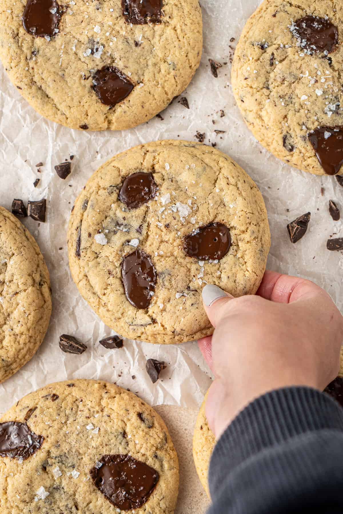 A hand picking up a dairy free giant chocolate chip cookie.