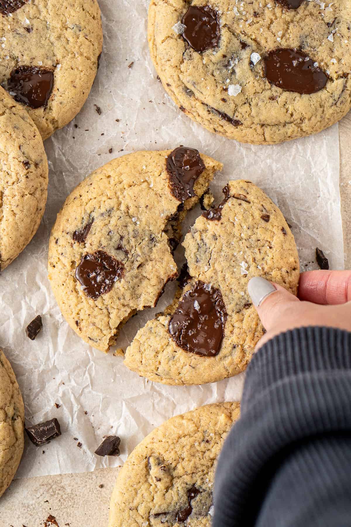A hand taking a half of a broken chocolate chip cookie.