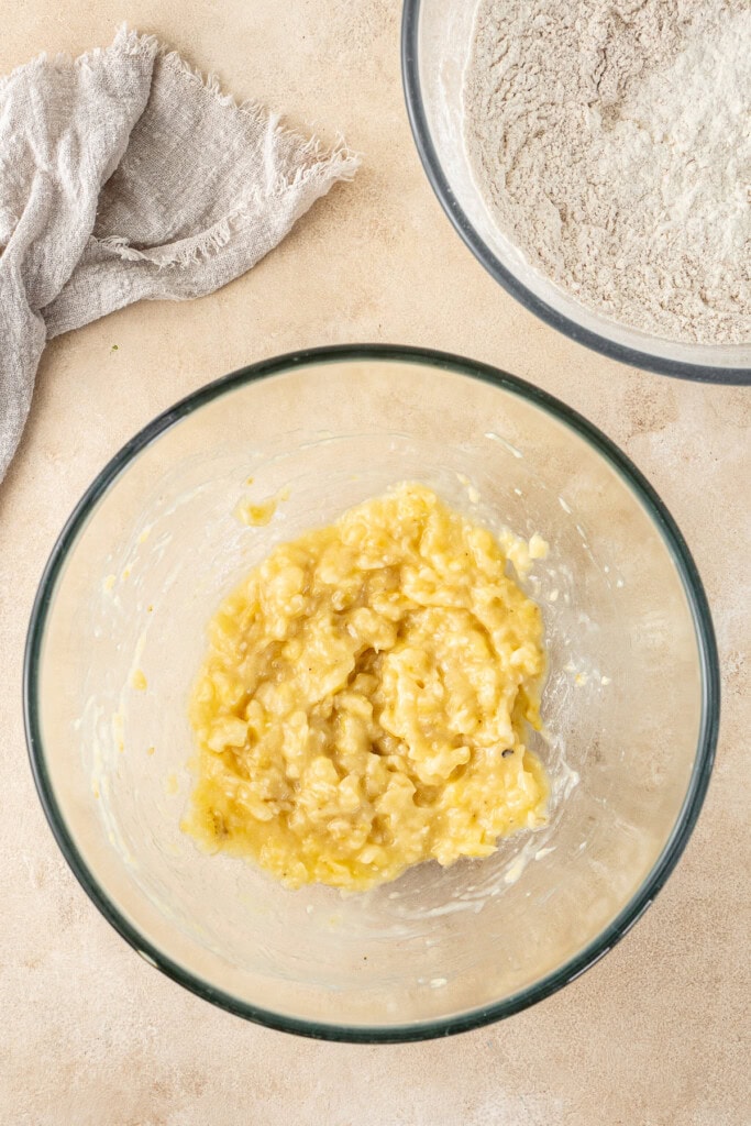 A bowl of mashed banana and another with the dry ingredients.