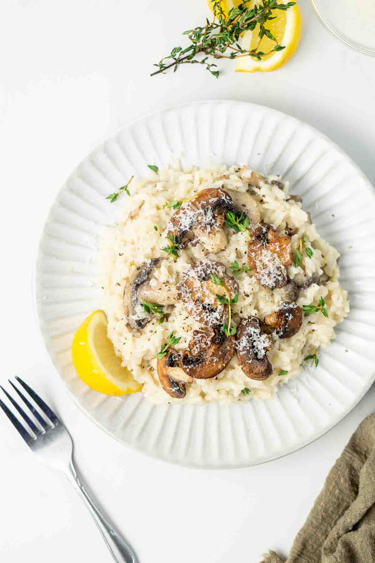Close up of mushroom risotto on a white plate with a slice of lemon and a fork.