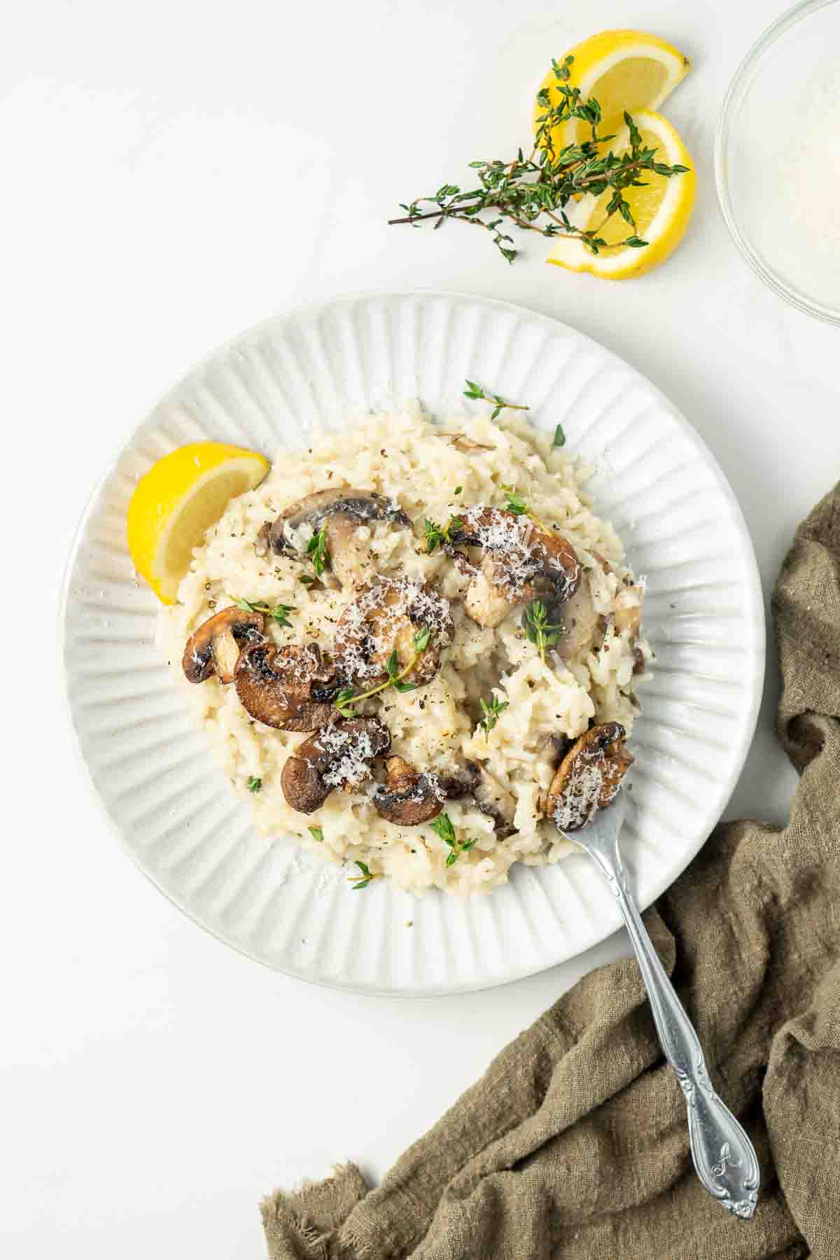Mushroom risotto on a white plate with a slice of lemon and a fork.