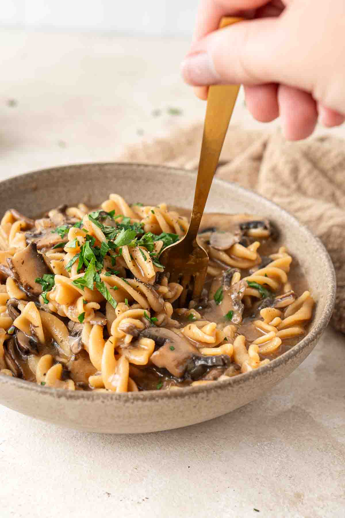 Close up of a fork taking a bite of mushroom stroganoff from a brown bowl.