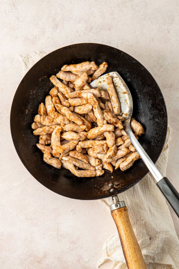 Stir frying the pork strips in the sauce.