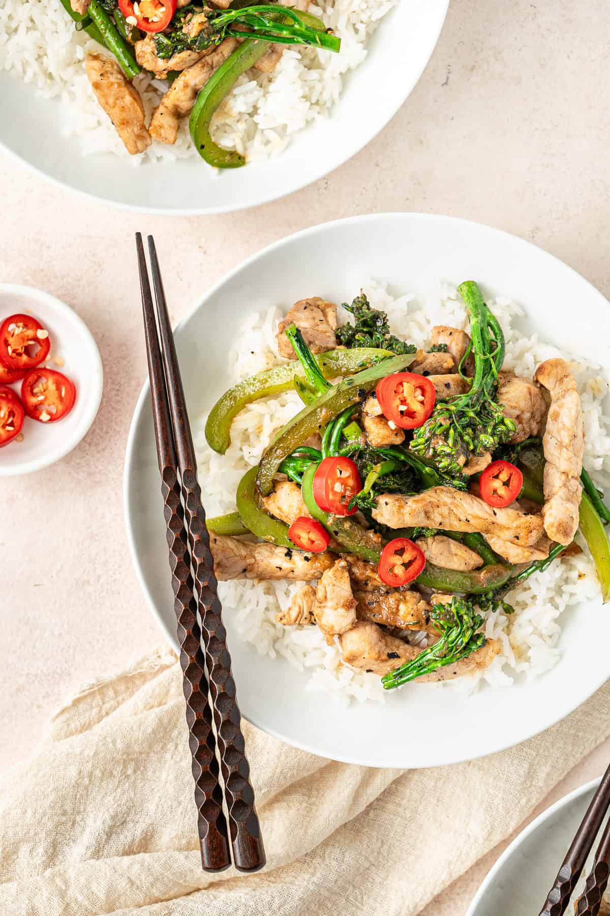 Hoisin pork stir fry over white rice in a white bowl with chopsticks.