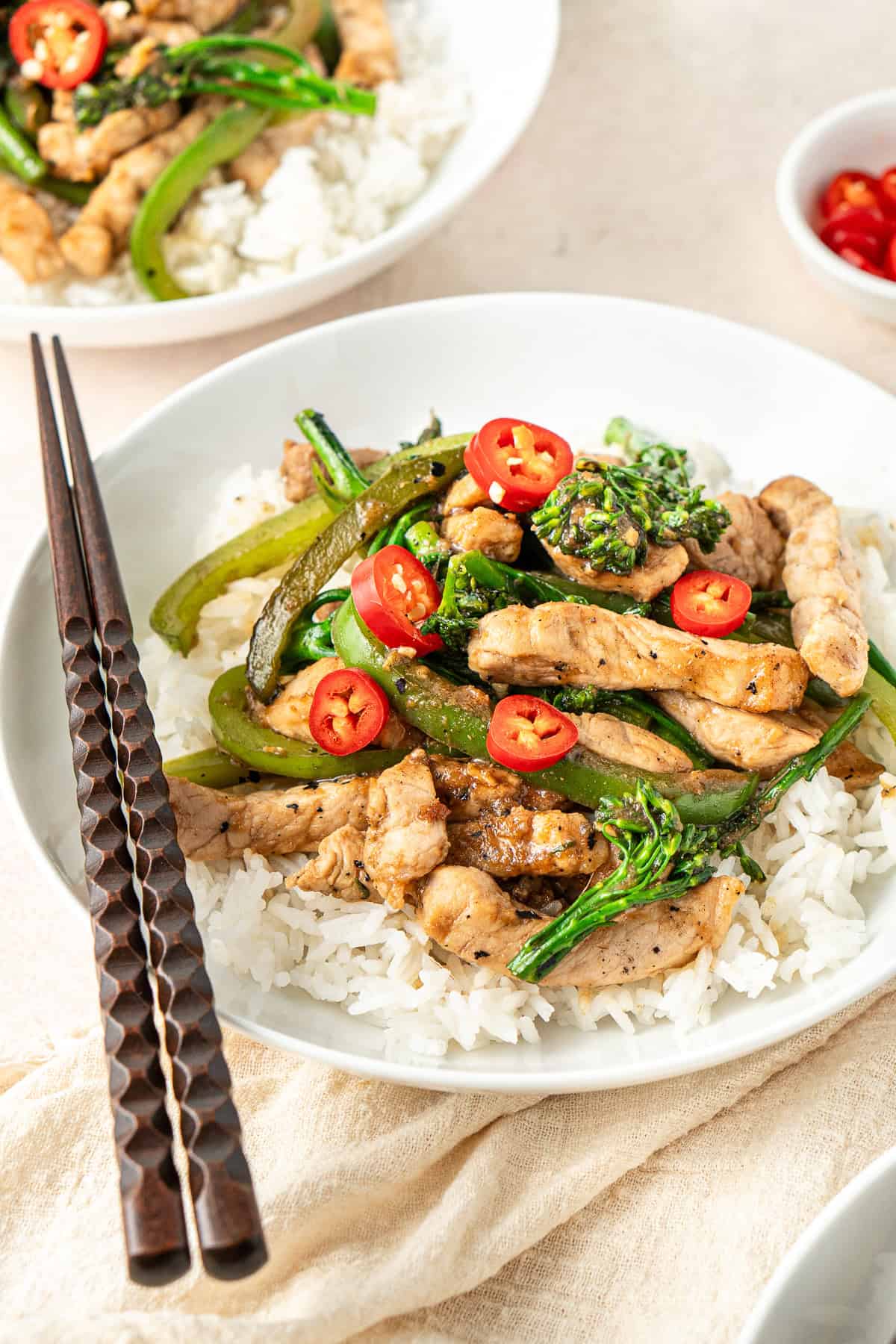 Close up of pork stir fry with hoisin in a white bowl with rice, topped with fresh chilli.