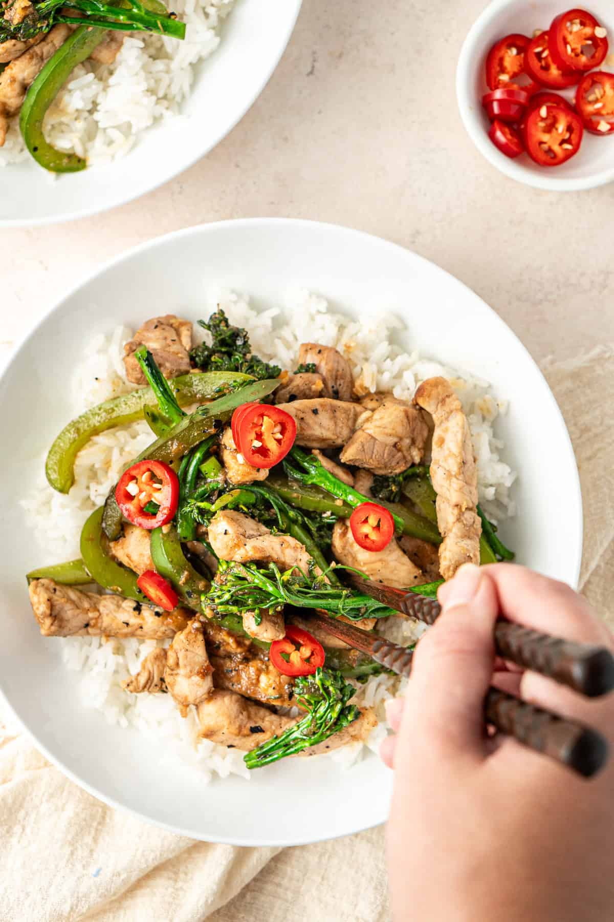 A hand with chopsticks taking a bite of the pork hoisin stir fry.