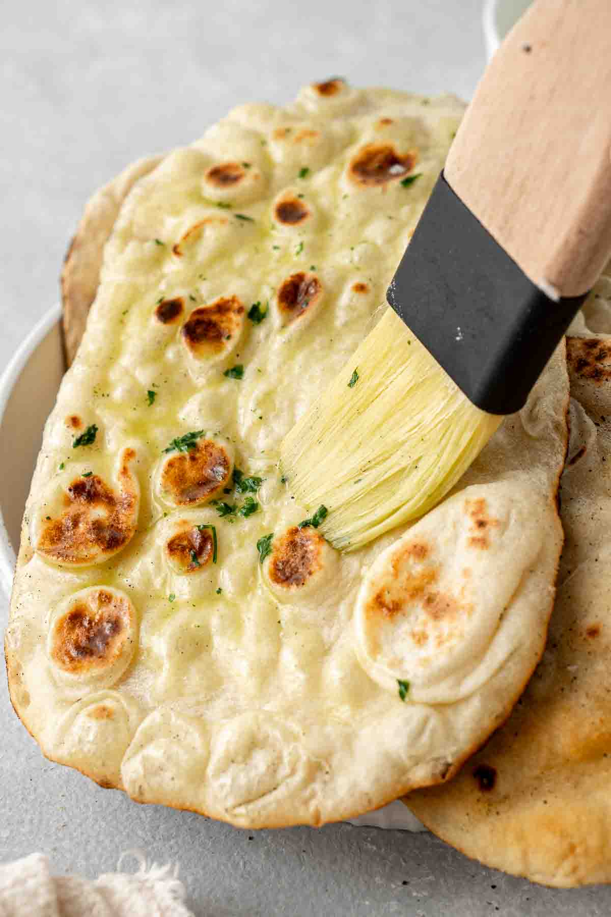 Pastry brush brushing garlic butter over freshly cooked naan.