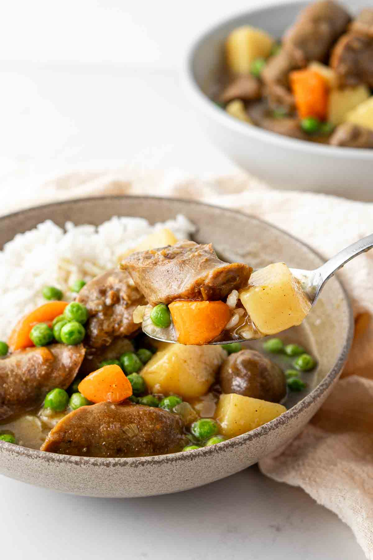 Spoonful of curried sausages in a bowl with rice.