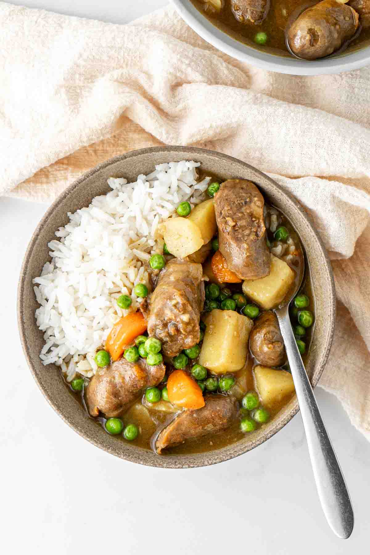 A bowl of slow cooked curried sausages served up with rice and a spoon.