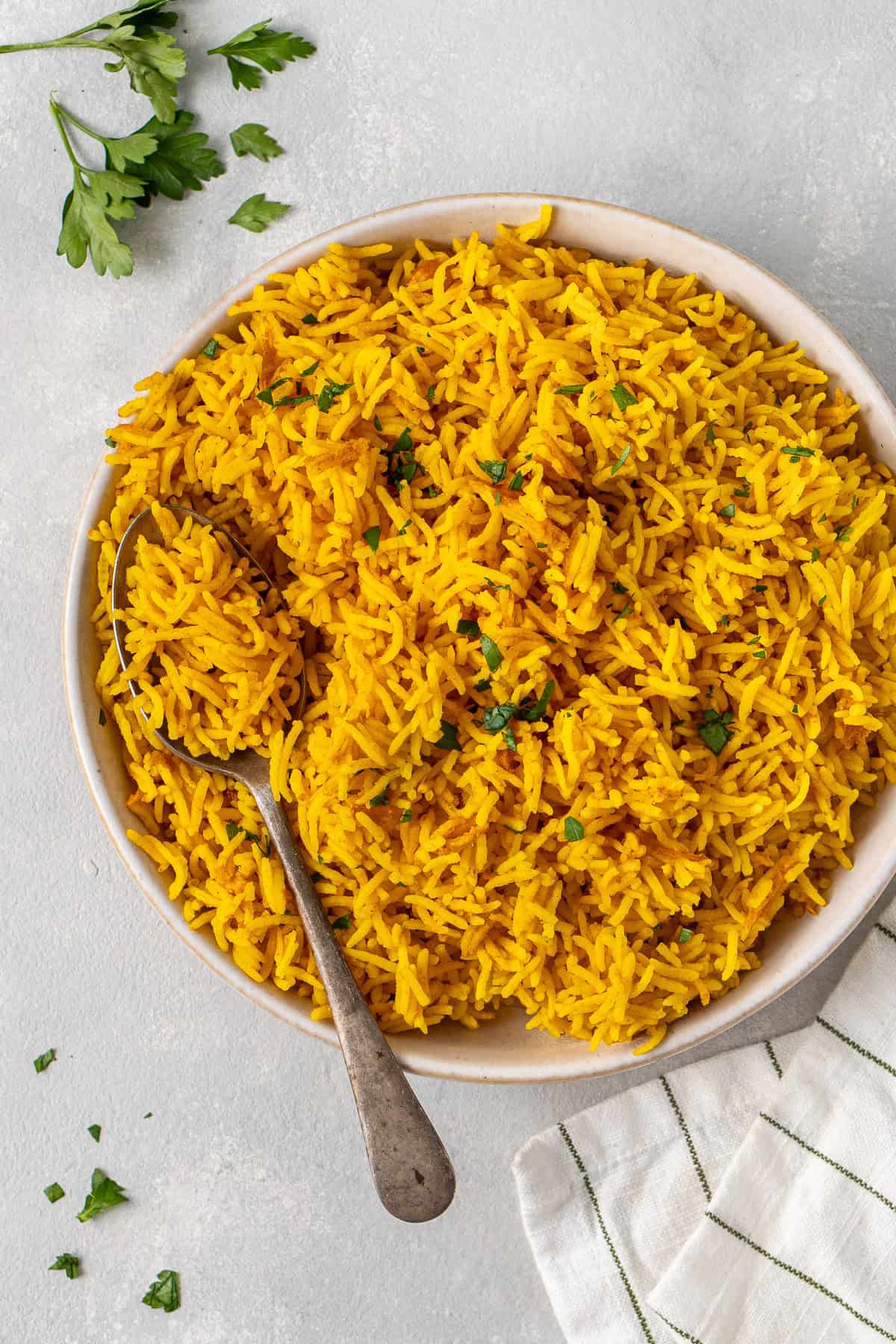 Close up of a white bowl of turmeric rice with a serving spoon.