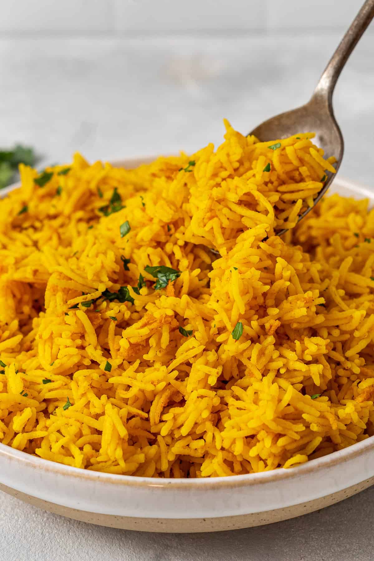 A spoon serving the yellow rice from a white plate.